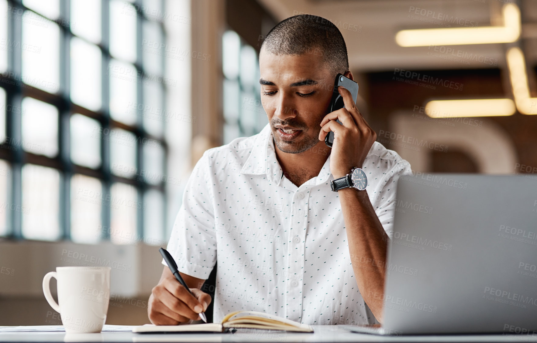 Buy stock photo Shot of a young businessman using a laptop, smartphone and making notes in a modern office