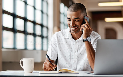 Buy stock photo Shot of a young businessman using a laptop, smartphone and making notes in a modern office