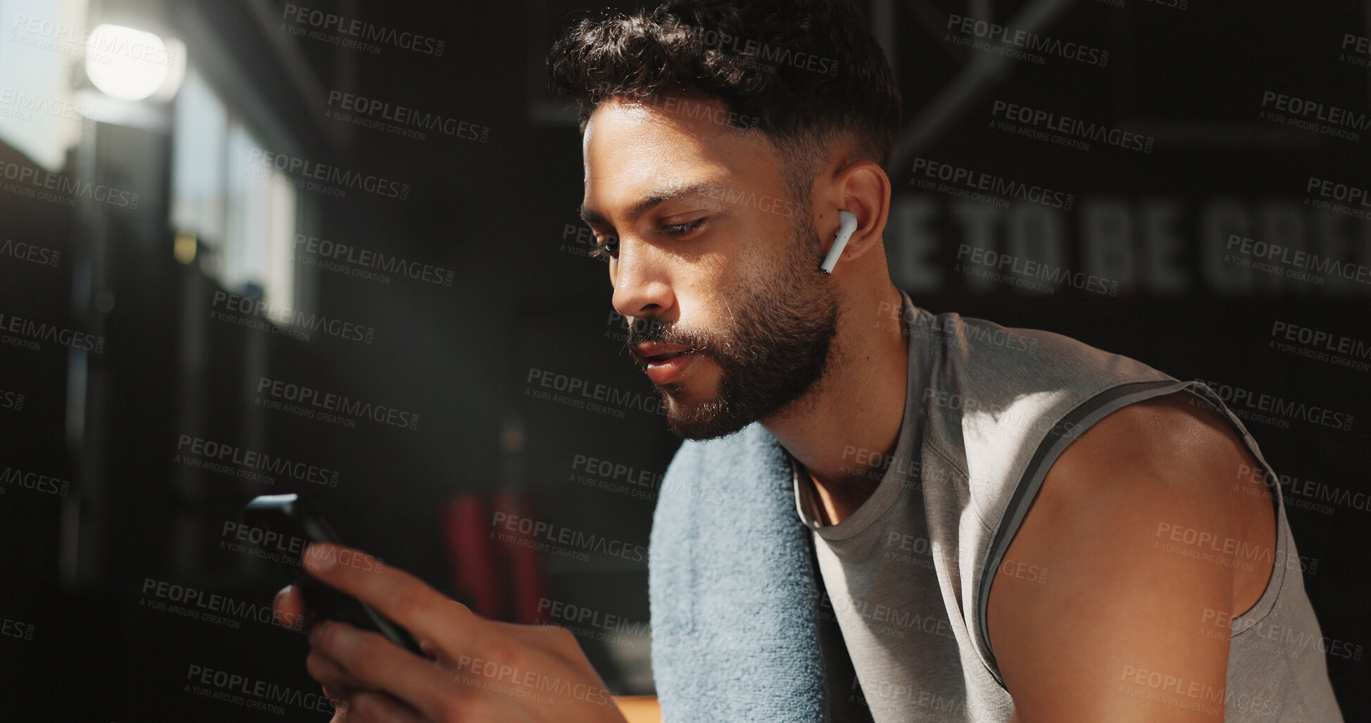 Buy stock photo Man, earphones and phone in gym for fitness, check wellness app or health stats with connection. Person, audio and technology for tracking exercise goals, sports podcast and internet with training