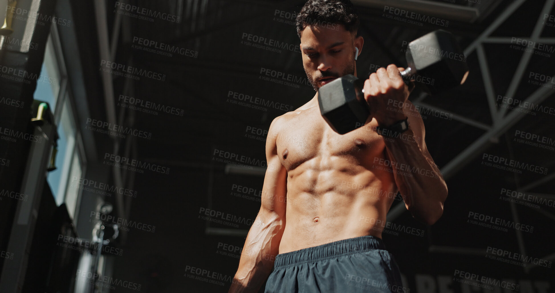 Buy stock photo Dumbbells, fitness and bodybuilder man with music and serious for training, muscle growth and self care. Earphones, workout playlist and person or low angle in gym for exercise, strong and power