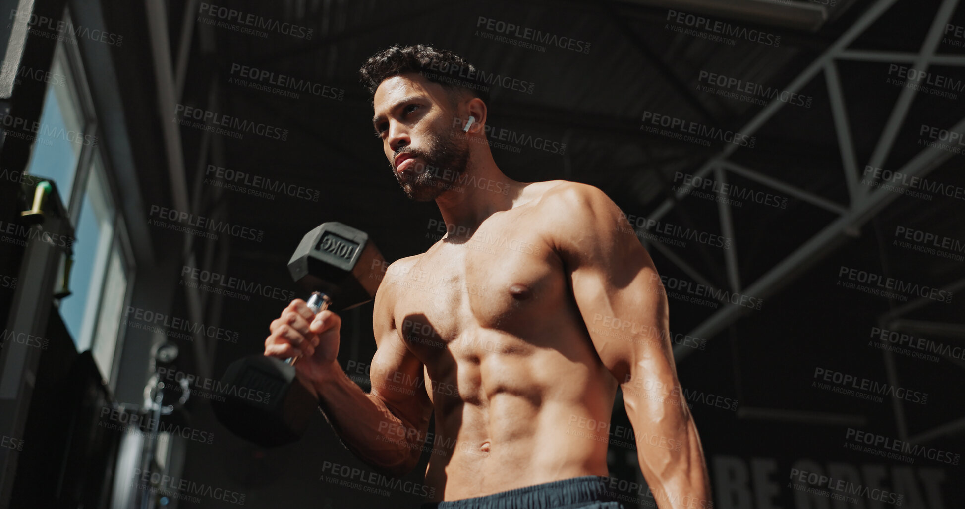 Buy stock photo Dumbbells, gym and bodybuilder man with music and serious for training, muscle growth and self care. Earphones, workout playlist and person or low angle of exercise for fitness, strong and power