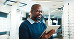 Optometry, typing and man on tablet for store inventory, stock and checklist for frames. Shop, mature and African person on digital tech with prescription lens, spectacles and glasses for vision
