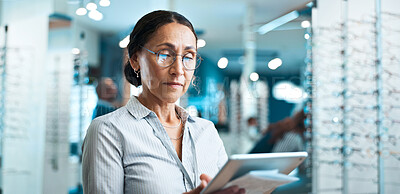 Buy stock photo Glasses, woman or tablet in shop for eye care, order custom lenses or process insurance claims. Optical assistant, eyewear and mature person with app for stock check, online inventory or product info