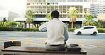 Man, waiting or checking time on bench in city for public transportation, travel or outdoor lift. Back view, male person or civilian with commute delay for bad schedule, departure or trip on sidewalk