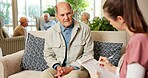 Elderly, man and discussion with nurse in retirement home for healthcare, routine or schedule. Woman, caregiver or senior male person on sofa for daily agenda, planning or checklist in old age house