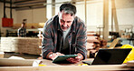 Carpenter, scroll and man with tablet in workshop, online and searching for furniture design on web. Warehouse, artisan and mature person with technology, research or planning for woodworking project