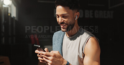 Buy stock photo Man, phone and earphones in gym with fitness app, smile and listen to online music playlist in break. Happy, person and exercise recovery in health club with audio tech, radio and send text message.