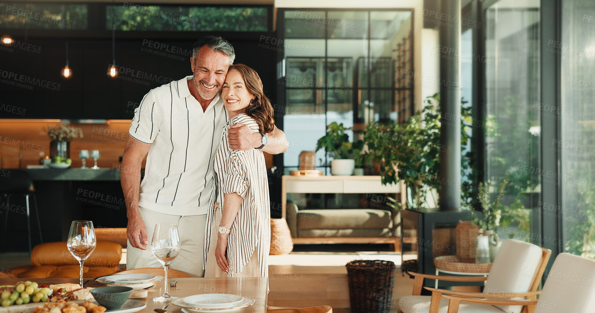 Buy stock photo Happy, couple and hug in house with lunch, wellness and love for bonding together on weekend break. Portrait, mature people and embrace by dining table with meal, companion or smile for relationship.