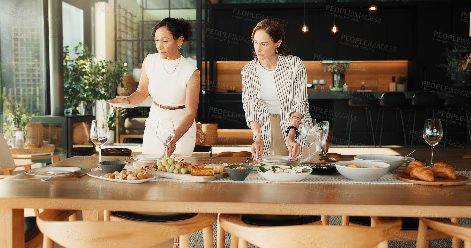 Buy stock photo Friends, host and help with food in home for social event, meal or dining table setting. Mature women, serious and together in house with healthy snack, brunch or talking dietary for party catering