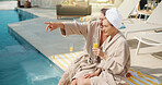 Couple, talking and drinks at resort for travel, sightseeing and bonding together on holiday. Mature people, pointing or orange juice at poolside with partner, discussion and outdoor view on vacation