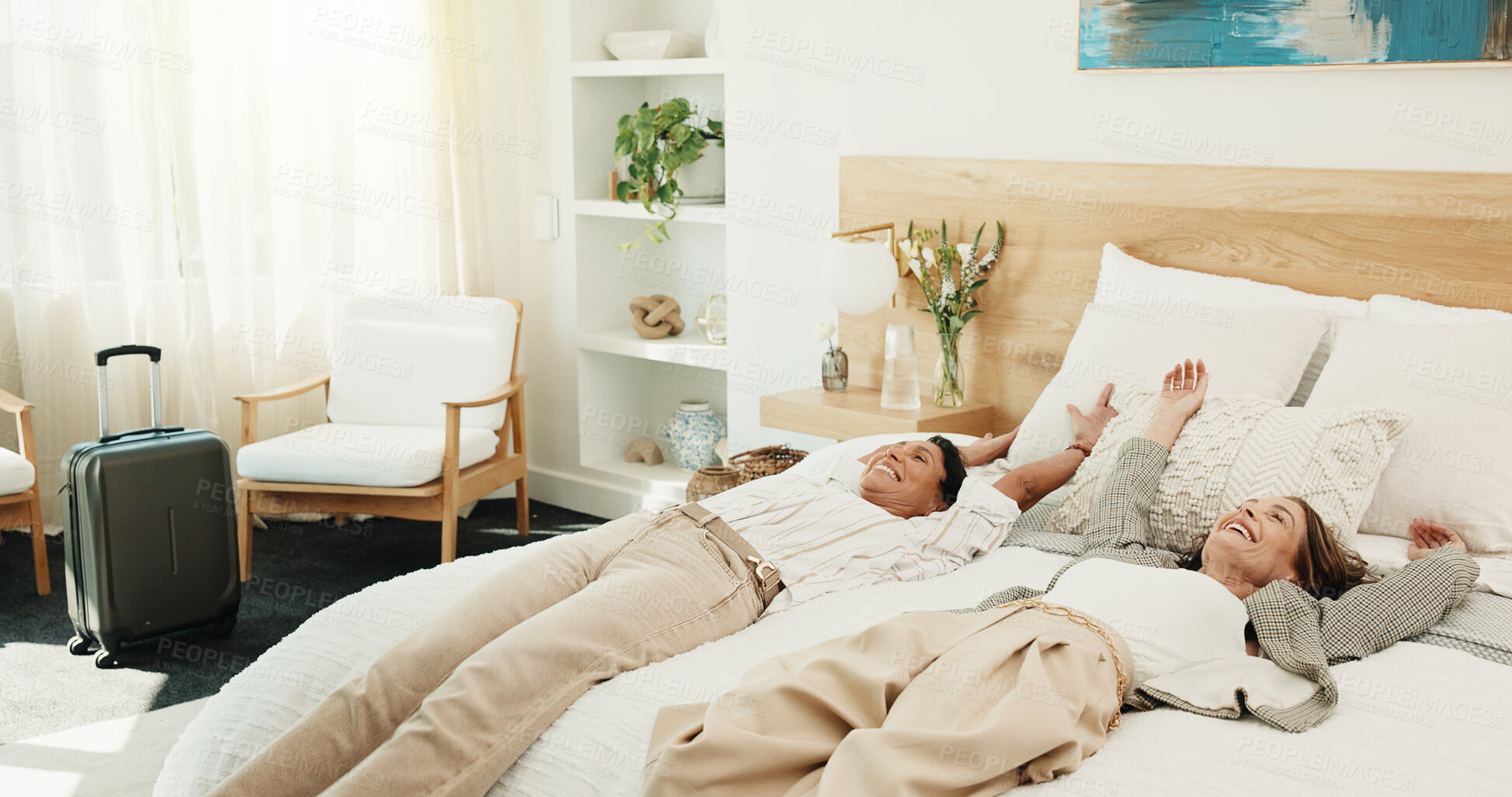 Buy stock photo Happy, women and relax with suitcase in bedroom hotel for holiday, weekend getaway or vacation. Female people, lying or accommodation with smile in bed for break, rest or bonding together in resort
