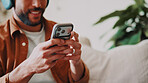 Man, hands and music or phone on home sofa for streaming, podcast or online audio subscription. Smile, headphones and male person relax on couch with mobile app, technology and typing for sound