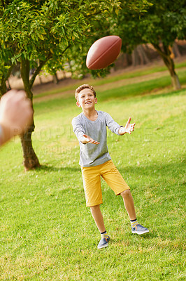 Buy stock photo Happy child, outdoor and catch ball with people for playing sport, physical activity and skill development. Boy, kid smile and practice for game, American football training and wellness in nature.