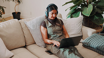 Buy stock photo Woman, headphones and remote work in home with laptop, check AI copywriting draft or listen to music. Freelance copywriter, person and typing on sofa with computer, audio tech and streaming radio.