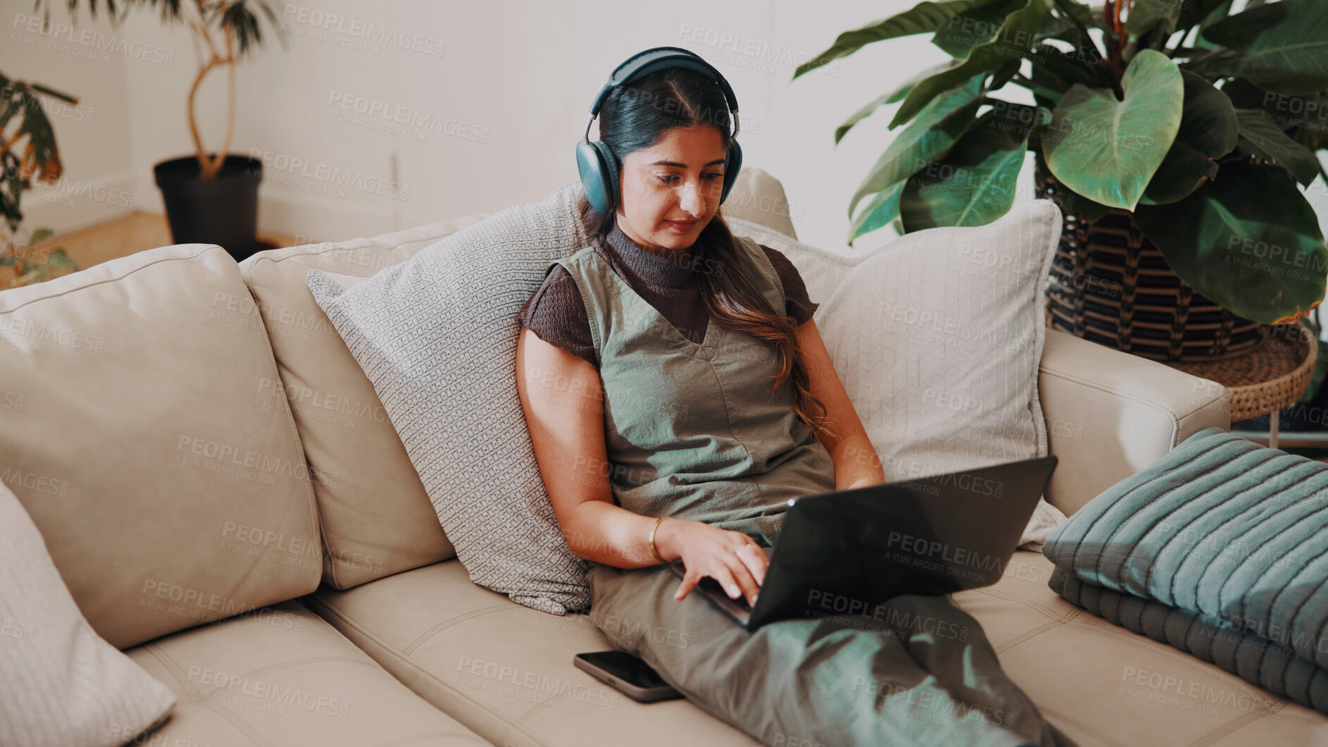 Buy stock photo Woman, headphones and remote work in home with laptop, check AI copywriting draft or listen to music. Freelance copywriter, person and typing on sofa with computer, audio tech and streaming radio.