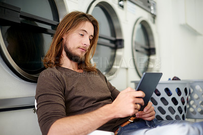 Buy stock photo Laundromat, relax and man with tablet, waiting and connection for social media, patience and text. Person, cleaning and washing clothes with technology, chore and message with online game or internet