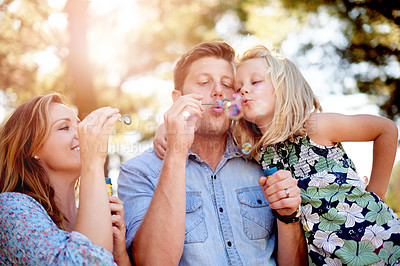 Buy stock photo Smile, family and daughter blowing bubbles in nature, bonding together or playing for connection. Happy, parents and child outdoor with flare, summer activity and childhood memory on weekend break.