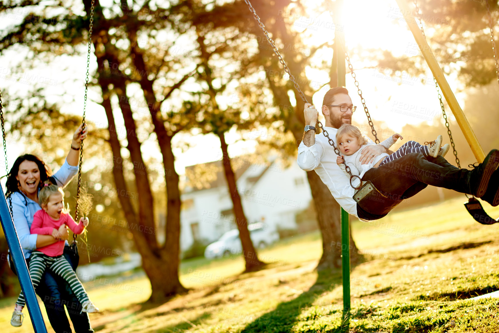 Buy stock photo Nature, swings and parents with children in park for holiday, weekend or vacation together. Smile, trees and kids with mother and father for playing outdoor on playground for connection in summer.