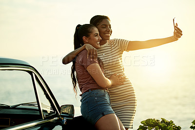 Buy stock photo Shot of two young women taking selfies with a mobile phone on a road trip