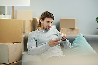 Buy stock photo Man, smartphone and earphones on sofa, new home and streaming video tutorial for interior design in lounge. Person, phone and mobile app with music, subscription or moving with boxes at apartment