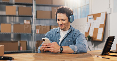 Buy stock photo Logistics, man and headphones in office with phone, streaming music and check mobile app for order. Happy, person and ecommerce in depot with audio tech, track courier online and listen to podcast.