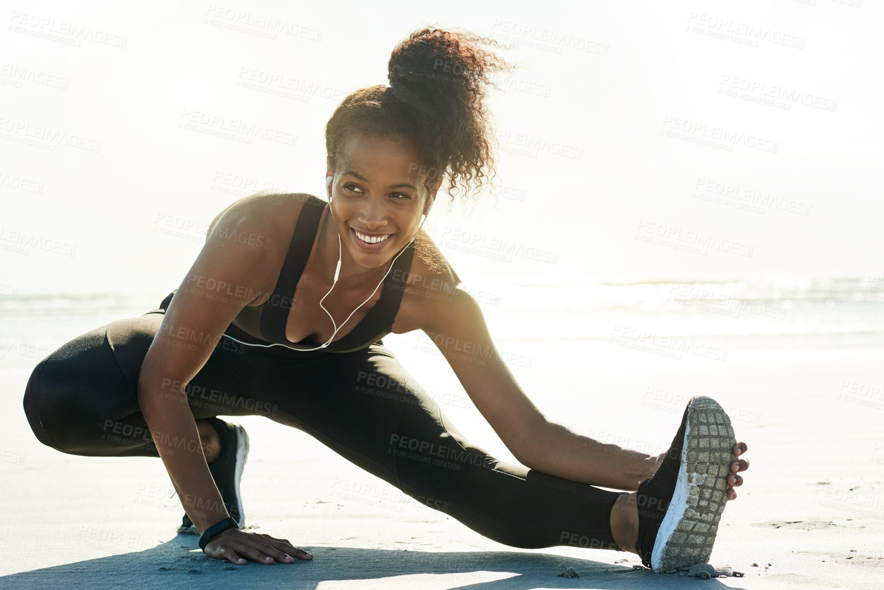 Buy stock photo Happy woman, fitness and stretching leg with earphones on beach for workout preparation in nature. Active, female person or runner with smile for warm up, flexibility or start exercise on ocean coast