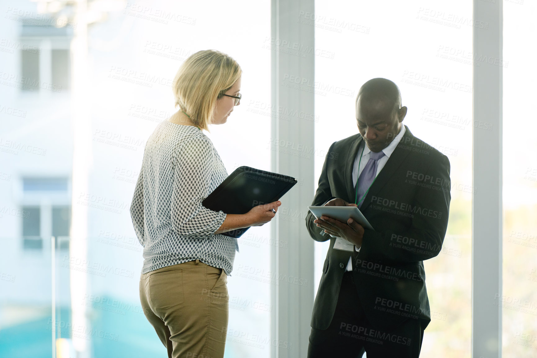 Buy stock photo Collaboration, manager or employee at window with tablet for feedback, communication or project review. Digital app, discussion or business people in workplace with tech, teamwork or strategy meeting