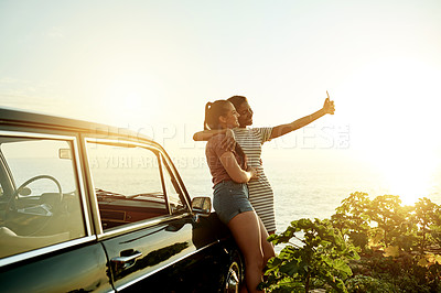 Buy stock photo Shot of two young women taking selfies with a mobile phone on a road trip