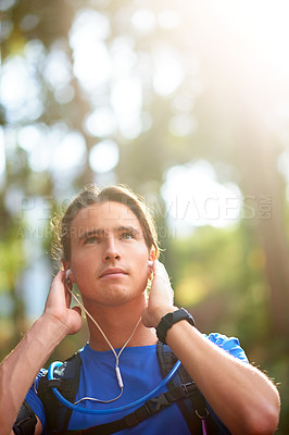 Buy stock photo Music, hiking and relax with man in nature for wellness podcast, streaming and health. Exercise playlist, trekking and adventure with person and earphones in forest for audio, subscription and peace