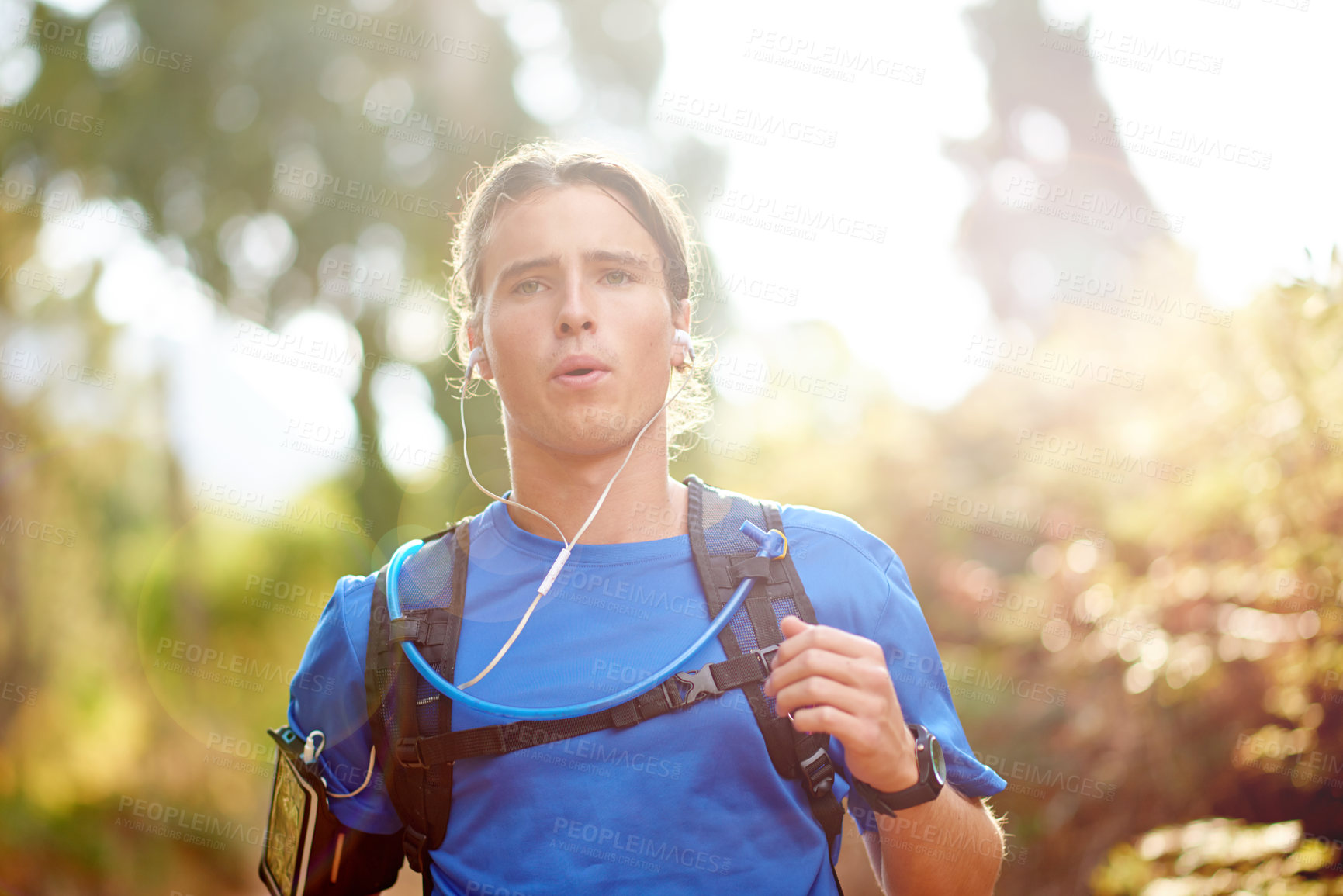 Buy stock photo Fitness, man and running with earphones in forest for marathon training, cardio podcast or breathing exercise. Runner, energy and backpack on mountain trail for workout performance, music or playlist
