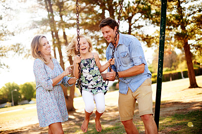Buy stock photo Parents, child and happy on swing at park for playing together, freedom and holiday weekend. Family fun, people and riding on playground equipment for bonding, sensory stimulation or childhood memory