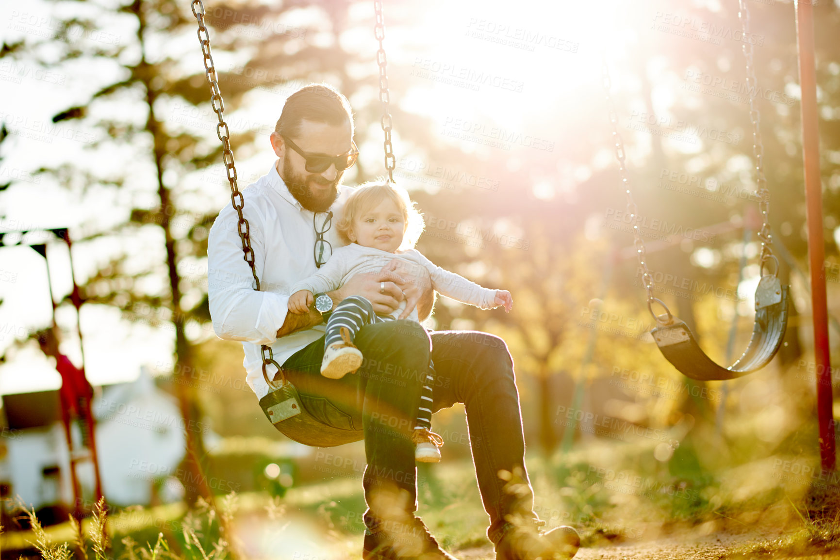 Buy stock photo Sunlight, swing and dad with child in park for playing, fun and bonding on weekend in nature. Happy, family and father with girl on playground for relationship, holiday and adventure together outdoor