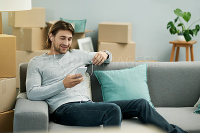 Buy stock photo Man, phone and smile on sofa in new home, earphones and listen to music with texting on web in lounge. Person, smartphone and mobile app for streaming subscription, moving and boxes at apartment