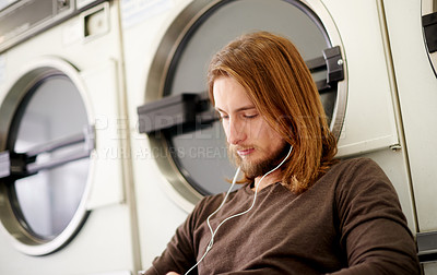 Buy stock photo Man, relax and washing laundry with earphones for listening to music, streaming podcast and laundromat. Male person, tech and audio with radio entertainment, cleaning service and maintenance routine