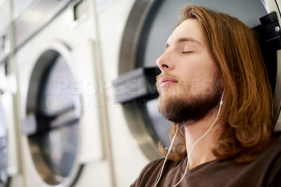Buy stock photo Relax, earphones and man by washing machine in laundromat listening to music, podcast or radio. Calm, laundry and male person with audio tech for streaming playlist or album with chores at shop.
