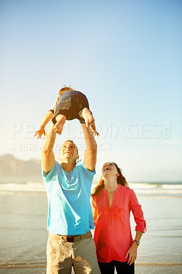Buy stock photo Beach, playing and parents with child in air for travel, bonding and relax outdoor on summer holiday. Family, happy and playful dad, mom and kid by ocean for adventure, vacation and weekend at space