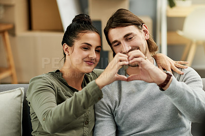 Buy stock photo New home, happy and couple with hands in heart for property, moving and house purchase. Homeowner, real estate and man with woman on sofa with love emoji for mortgage, investment and rental apartment