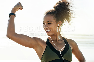 Buy stock photo Fitness, earphones and woman on beach with flex, strength and confidence with music. Pride, athlete and African bodybuilder with muscle growth by ocean, power and podcast for audio streaming.