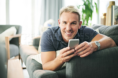 Buy stock photo Happy man, phone and portrait on sofa in home, relax and texting for online dating in lounge. Mature person, smartphone and laying on couch with mobile app, smile or social media at house in Spain