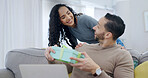 Couple, surprise and gift giving in home with smile for birthday celebration, care or appreciation. Wow, present and happy people on sofa for connection, gratitude and love on special day with laptop