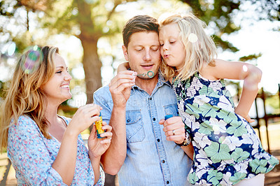 Buy stock photo Blowing bubbles, family and child in park for bonding, together and outdoor for fun. Soap toy, girl and parents in garden with mother, father and daughter with care and play in nature for weekend