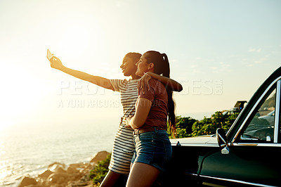 Buy stock photo Shot of two young women taking selfies with a mobile phone on a road trip