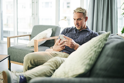 Buy stock photo Man, relax and scroll with smartphone on sofa, home and check notification with web chat in lounge. Mature person, phone and click with mobile app, contact and post on social media at apartment