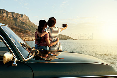Buy stock photo Shot of two young women taking selfies with a mobile phone on a road trip