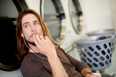 Buy stock photo Laundromat, man and earphones with sound, waiting and thinking with break, relax and radio. Cleaning, commercial machine and person with audio, listening to music and washing clothes with daydreaming