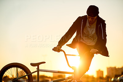 Buy stock photo Sunset, activity and man on bicycle in city with tricks, fun or skills for adventure with travel. Adrenaline, practice and person on bike training for competition, challenge or race in urban town.