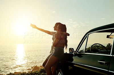 Buy stock photo Shot of two young women taking selfies with a mobile phone on a road trip