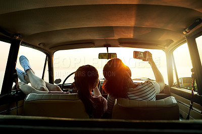 Buy stock photo Shot of two young women taking selfies with a mobile phone on a road trip