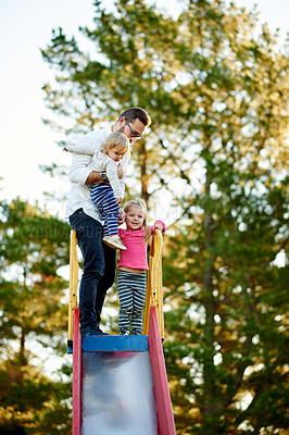 Buy stock photo Nature, slide and father with children in park for holiday, weekend or vacation together. Smile, trees and girl kids with dad for playing outdoor on playground for connection or bonding in summer.