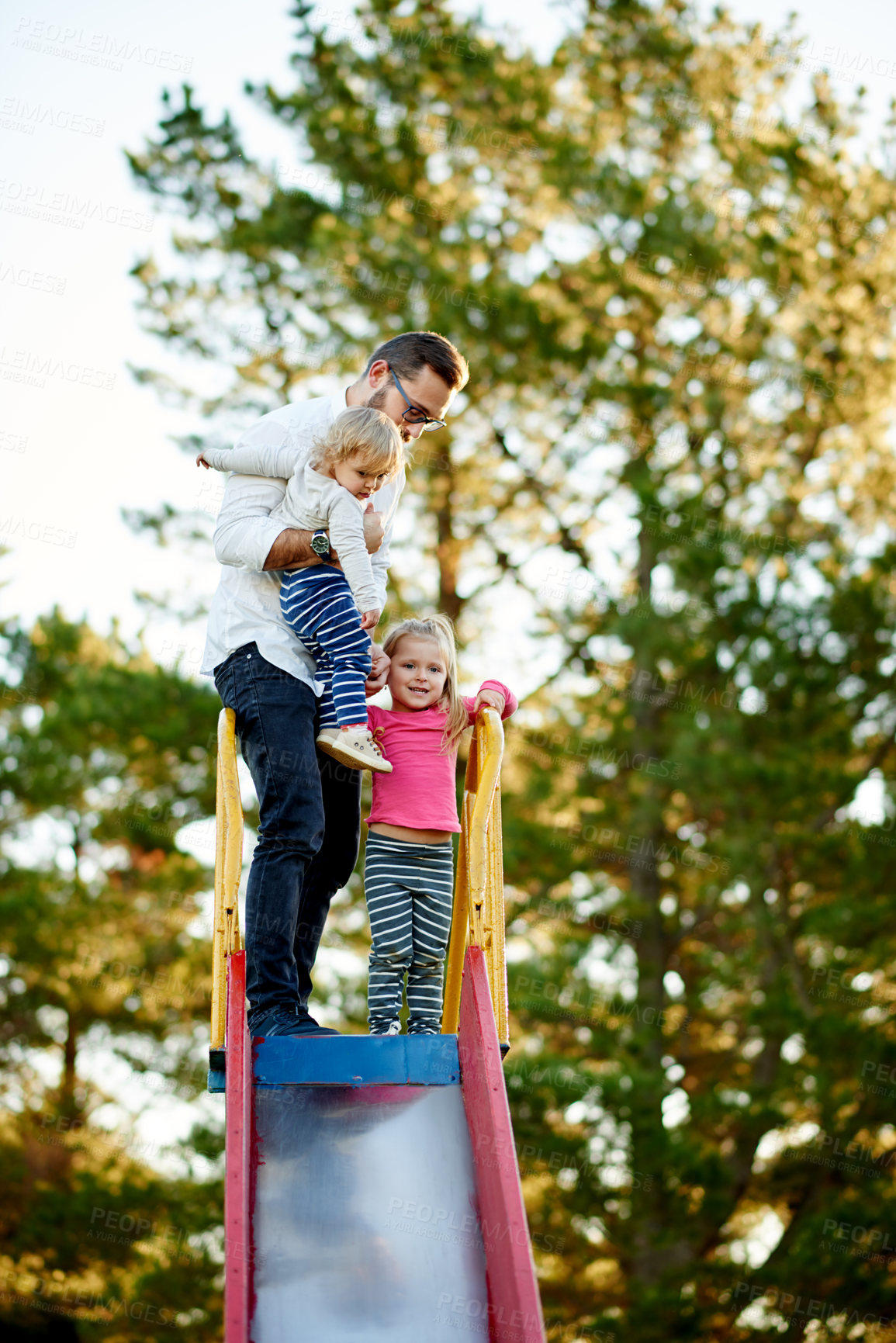 Buy stock photo Nature, slide and father with children in park for holiday, weekend or vacation together. Smile, trees and girl kids with dad for playing outdoor on playground for connection or bonding in summer.